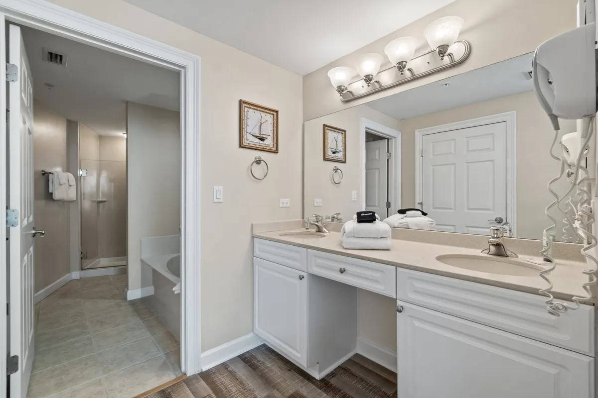 An elegant ensuite bathroom with a contemporary vanity area, large walk-in shower, and tasteful decorative wall art. The space feels inviting and spa-like, ideal for relaxation and self-care after a day in the sun.