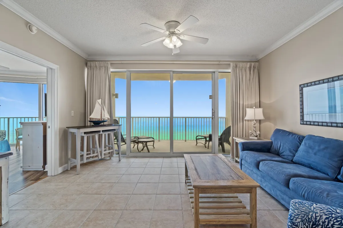 This inviting living space features a comfortable blue sofa, wooden coffee table, and decorative lamp, all oriented towards expansive windows that frame a breathtaking ocean view. The space exudes calm and is ideal for relaxing or engaging in games and conversation.