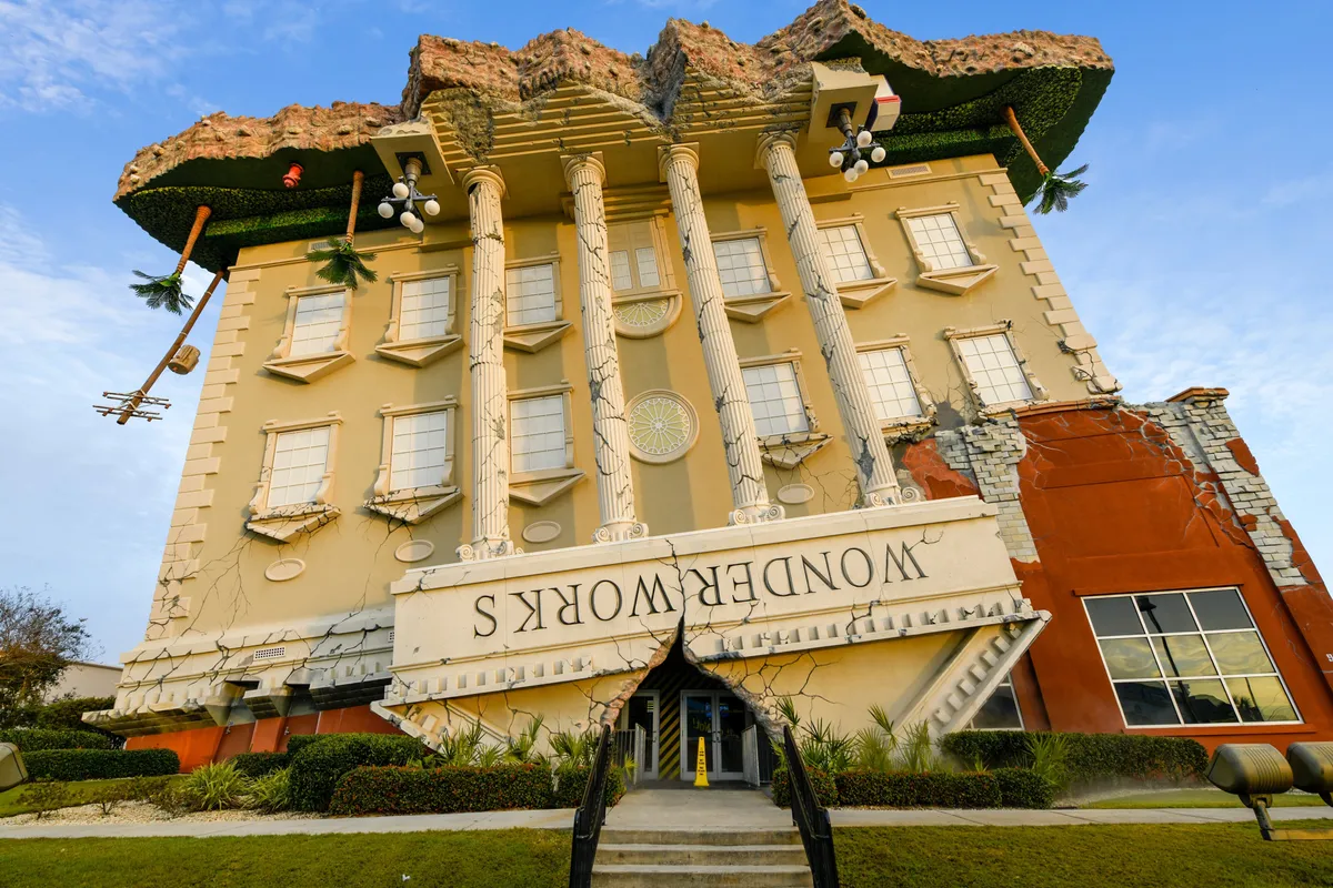 An exterior shot of WonderWorks, a whimsical, upside-down building adorned with tropical decorations and tall pillars, inviting curiosity and excitement. The unique architecture stands out as a playful local landmark, ideal for indoor exploration.